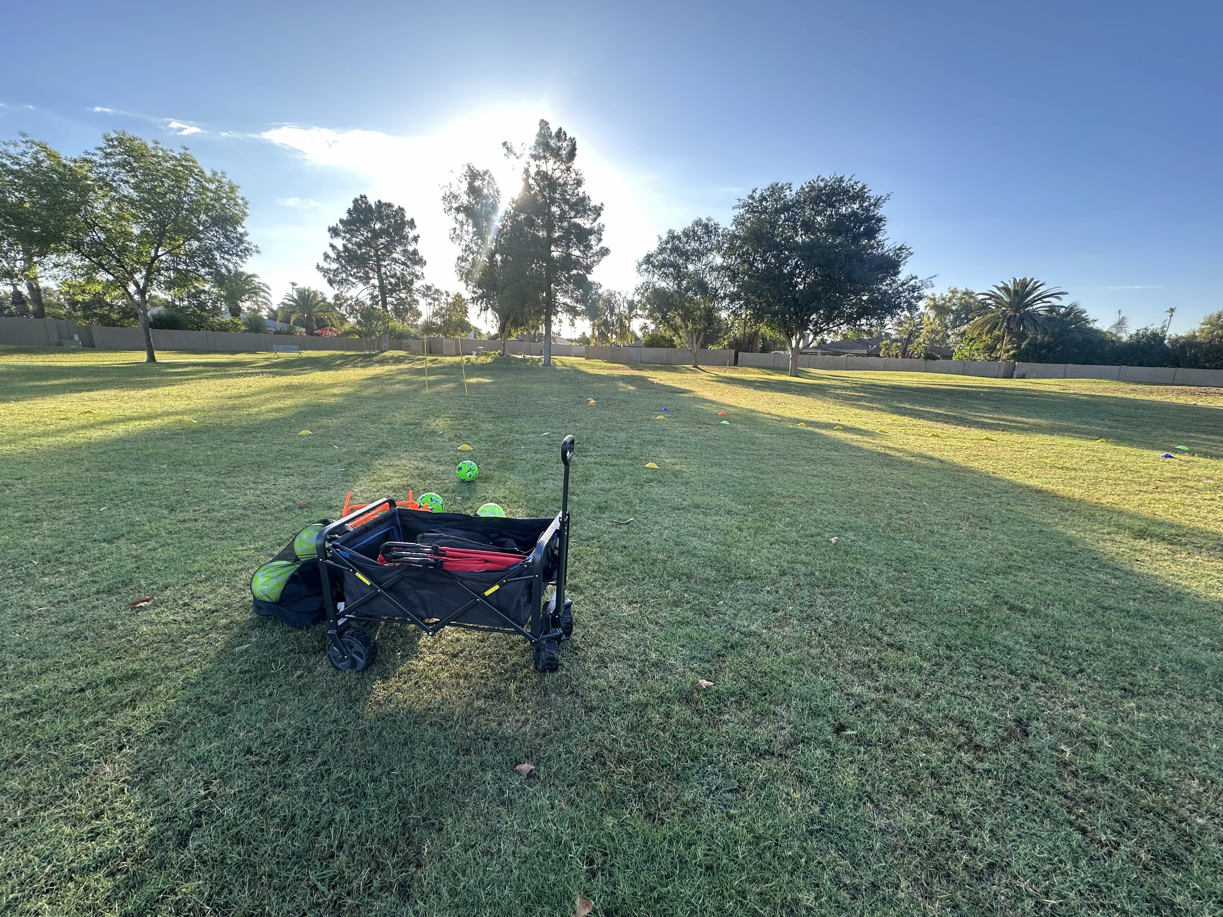 a wagon filled with training equipment and some soccer balls laying on a grass field in the early morning
